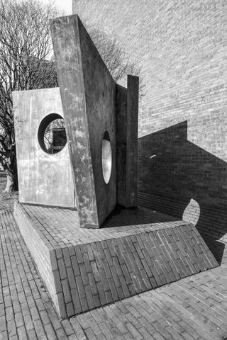 A black & white photo of a concrete sculpture. It looks like an open book with asymmetrical pages, with a hole in the middle of them.