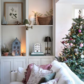 close up of alcove shelving and a built-in cupboard with festive decorations, beside a cream sofa and a pink decorated Christmas tree