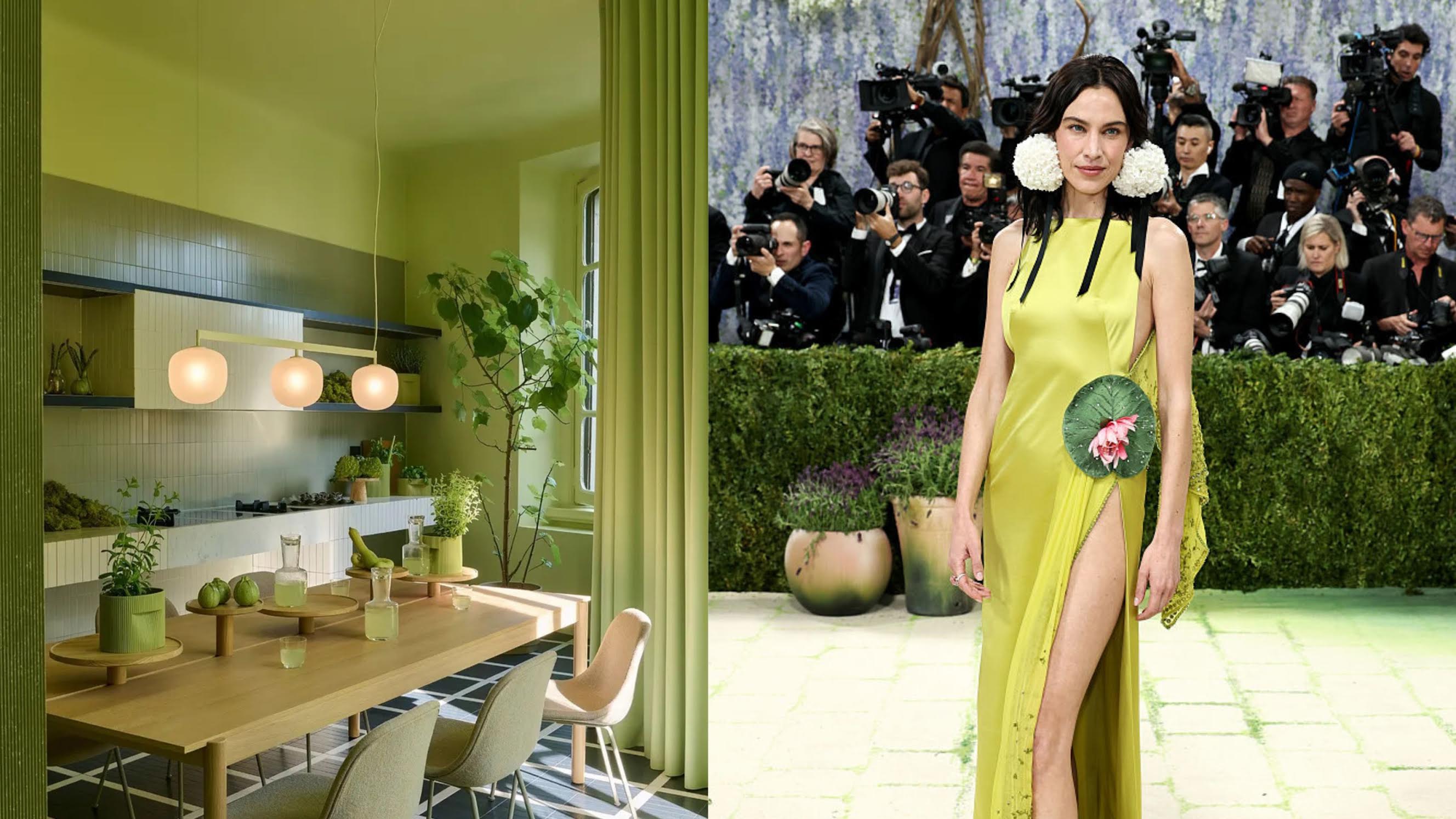 There is a table wooden table in a green tiled kitchen with three lights hanging over it. The floor is chequered black and white and on the table there are Apples, a carafe and plants.