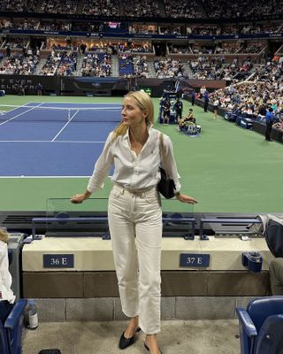 Woman wearing a white shirt and white jeans to a tennis match.