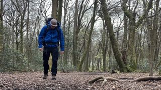 A man wearing a Revolution Race Aphex Pro walks through a forest.