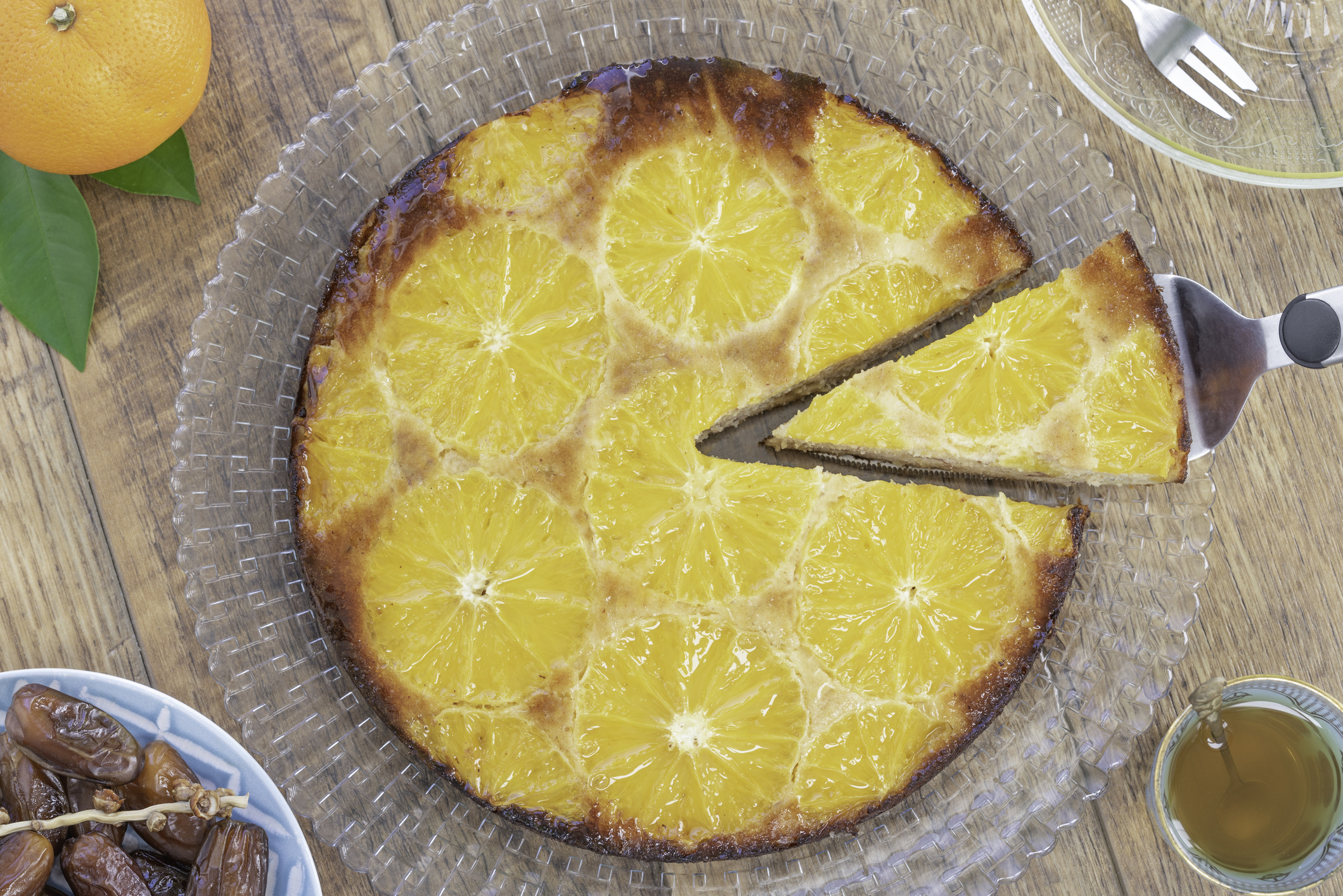 Homemade whole testy vanilla orange date upside down cake made from almond meal, eggs, dates and orange slices on the top and a drizzle orange syrup