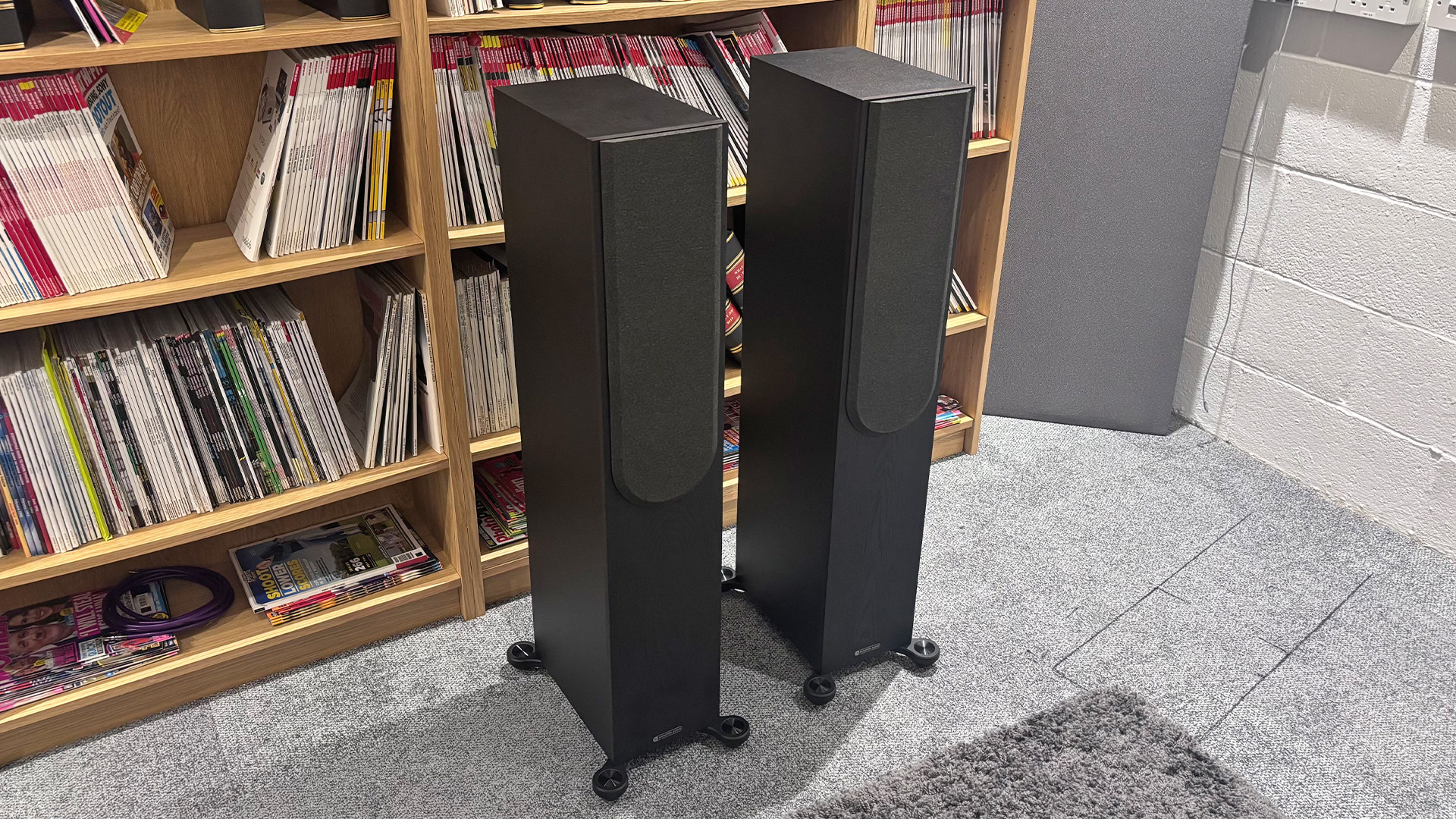 Monitor Audio Bronze 300 7G floorstanding speakers on grey carpet in front of bookcase with front grilles attached