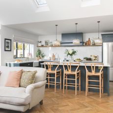 open plan blue kitchen extension with bar seating and grey sofa with wooden parquet floor