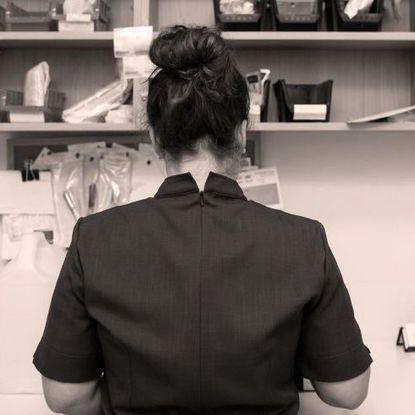 Sepia photograph of the back of a brunette lady wearing black with hair in a messy bun 