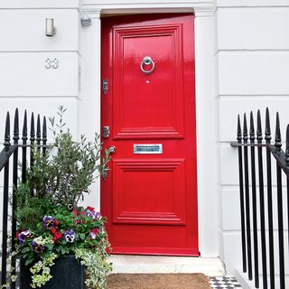 red front door with door mat and plants