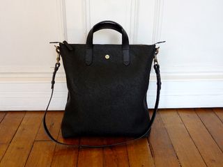 Luxury leather luggage from Mismo, Denmark. A deep black leather bag with hand and shoulder straps on a wooden floor.