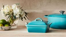 Le Creuset enamel Dutch oven and casserole dish in the Caribbean shade next to a vase of white flowers and a bowl of limes