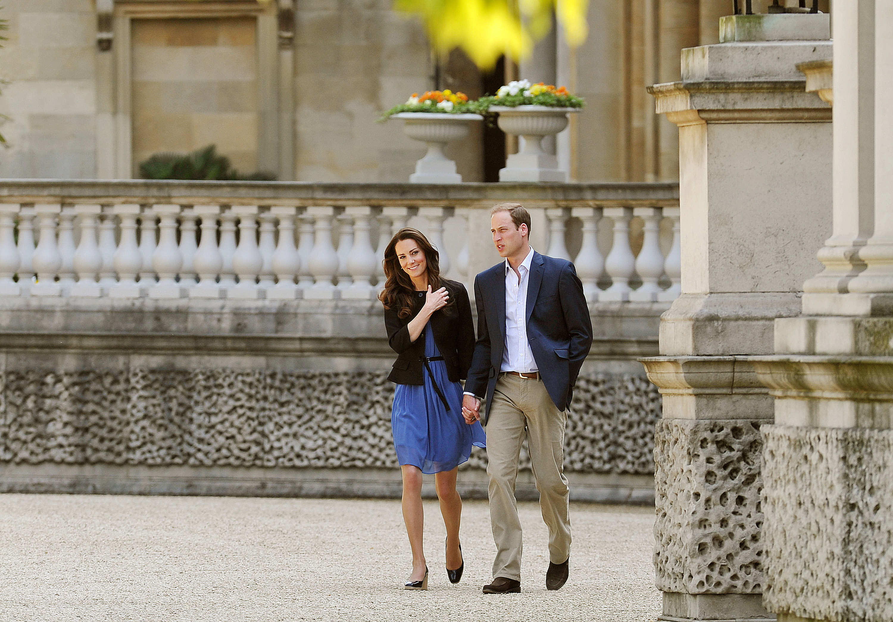 Princess Kate wearing a black blazer and blue dress holding walking next to Prince William