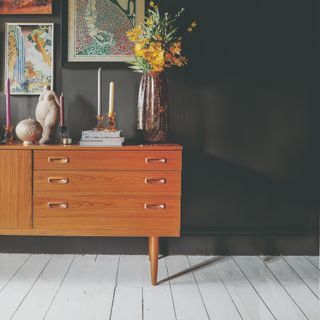 A living room with a mid-century sideboard, a black wall and a painted floor boards in white