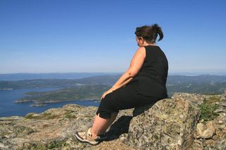 An overweight woman sitting outdoors on a rock.