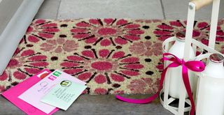 Pink floral doormat with pink letters and pints on milk on doorstep to show how to decorate a house after Christmas to make it feel more cheery