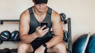 Man sat on weights bench in a gym looking at phone