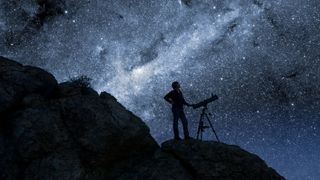 A stargazer stood on a rock with the night sky in the background