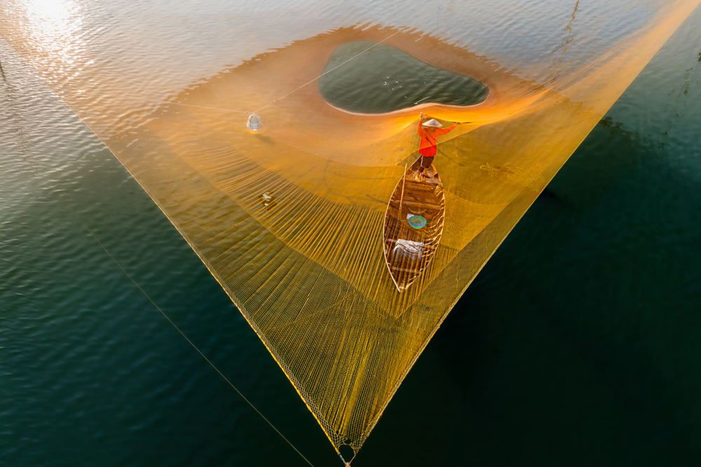 Fishermen casts net over canoe. 