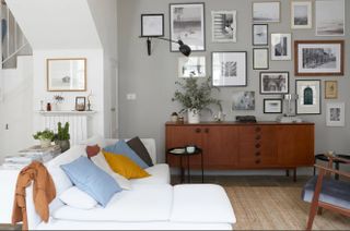 A living room with grey wall, gallery wall, wooden console and white sofa with blue, mustard, grey and white cushions