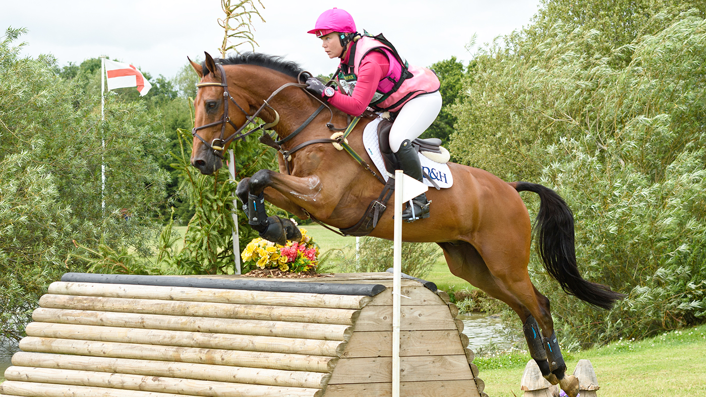 Nicole Mills jumps a roll top cross-country fence wearing bright pink colours on Fearless W.
