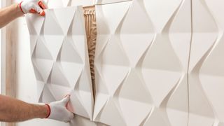 Installation of gypsum 3D panel. A worker is attaching the gypsum tile to the wall in a dining room.