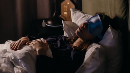 Woman sleeping in the dark under the covers wearing a sleep mask
