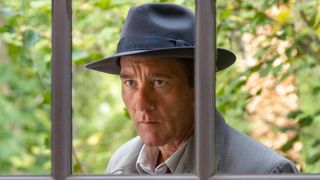 British actor Clive Owen, wearing trilby hat and grey jacket, peers intently between two metal bars in the new AMC TV detective drama