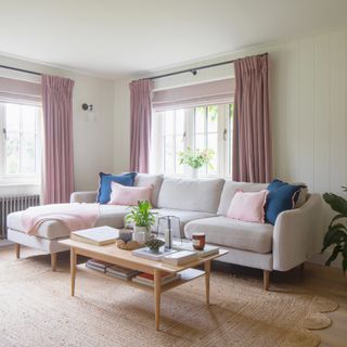 A living room with a grey chaise sofa with a pink throw and four cushions on a scalloped jute rug