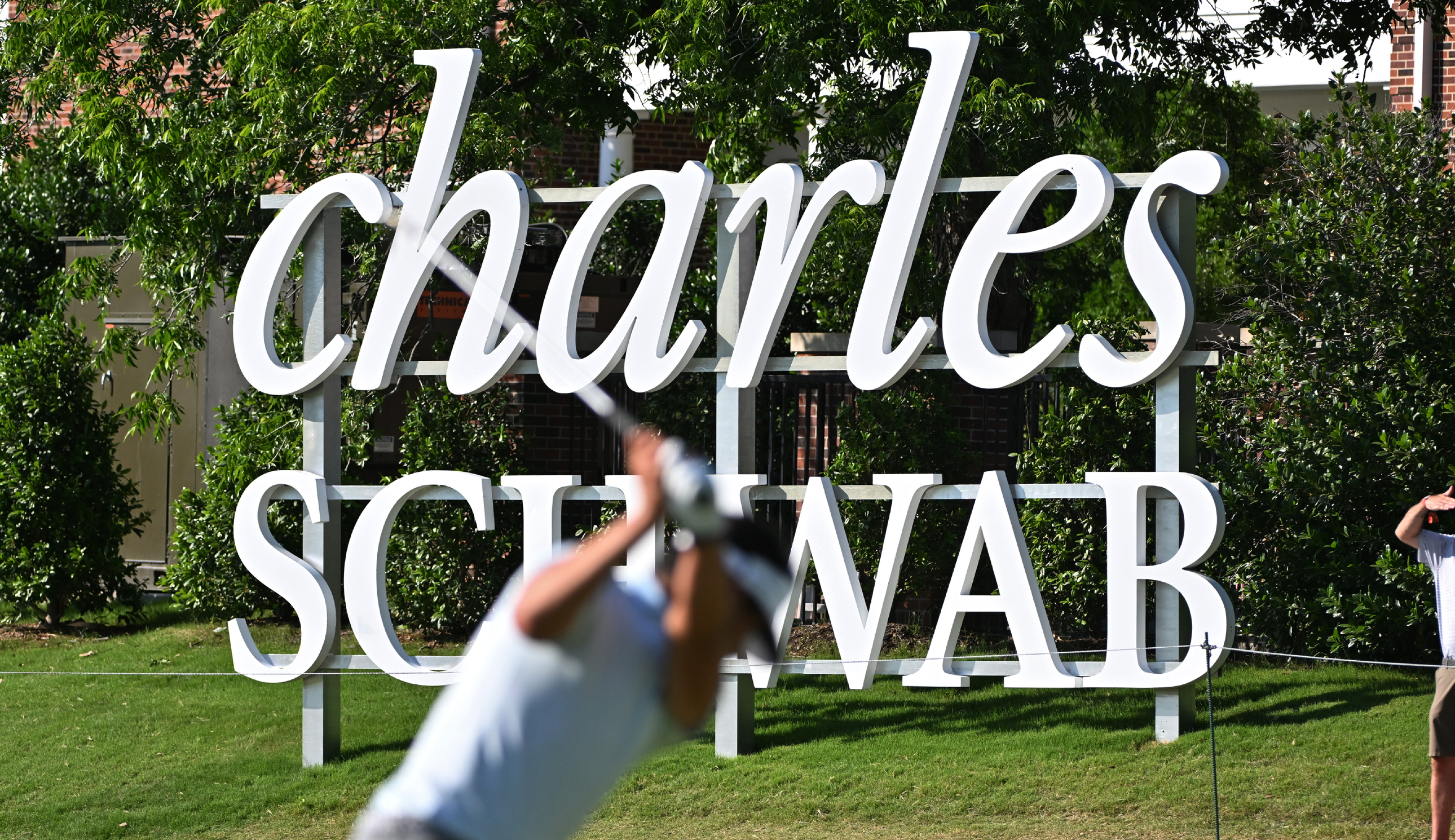 A golfer hits a shot in front of the Charles Schwab Challenge sign