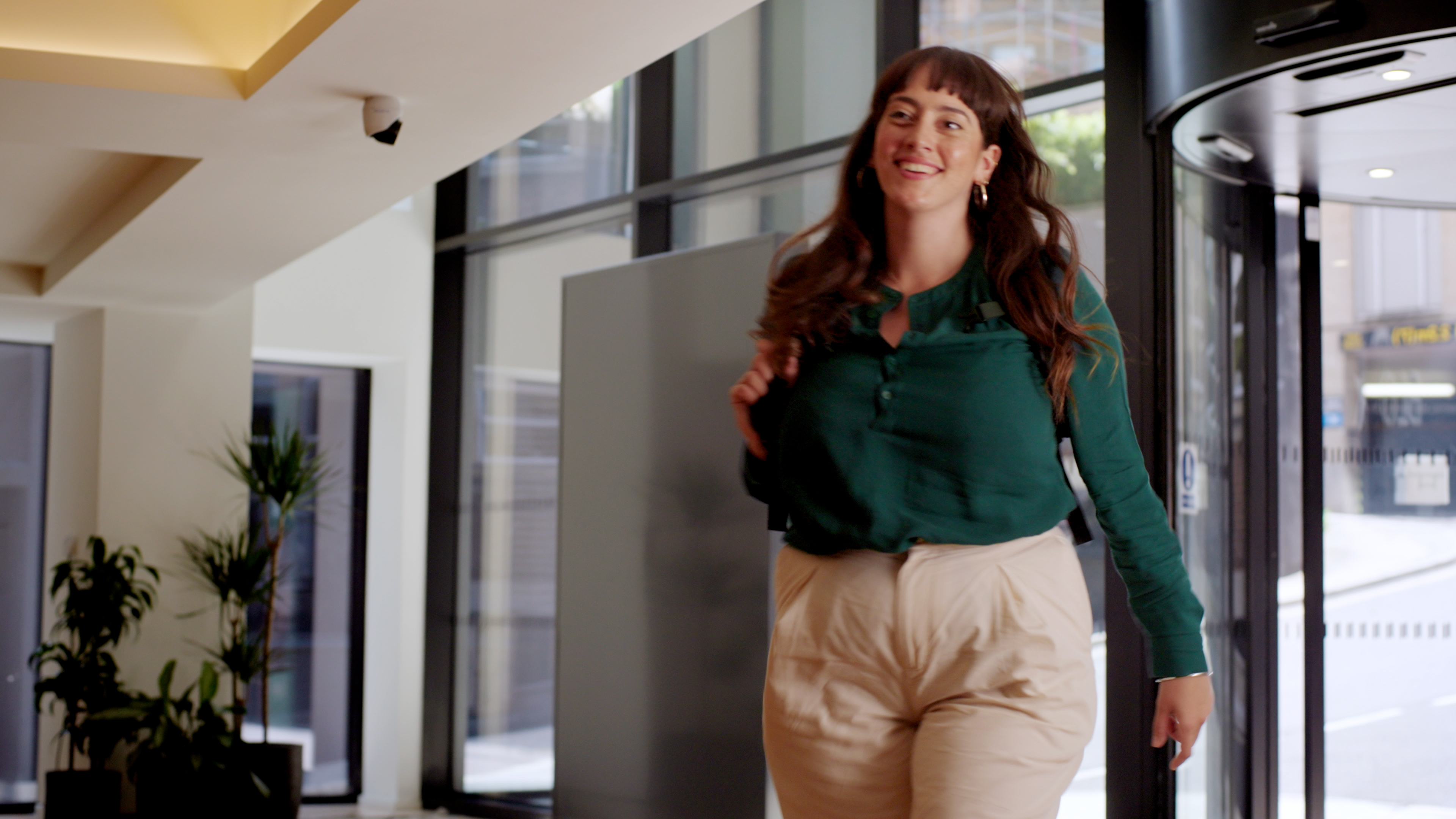 woman in green top and light trousers walking into an office