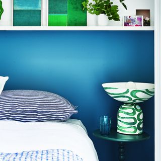 coastal bedroom idea with colour blocked blue walls, artwork on shelf, bright green artistic vase, stripe pillow