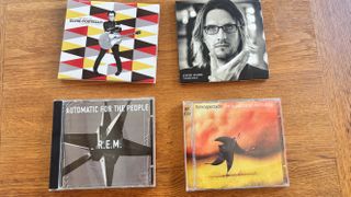 Four CDs on a wooden table, including REM, Elvis Costello and Supertramp