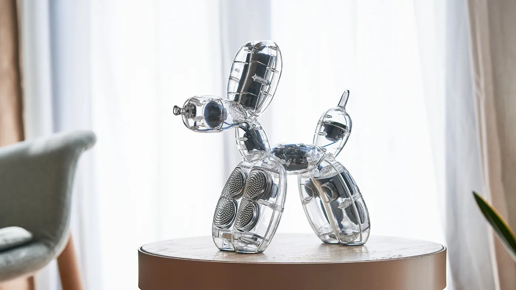 Lexon Balloon Dog Speaker shot in front of a net curtain and placed on a small round table