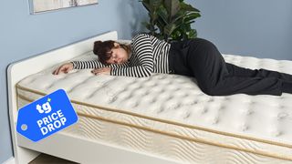 The image shows a dark haired mattress tester wearing a black and white stripey t-shirt and black trousers lying on her side on a cream and gold Saatva mattress