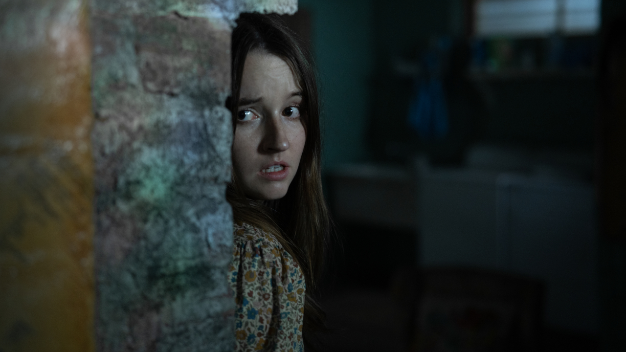 Kaitlyn Dever peeking around a corner with a scared expression in No One Will Save You.