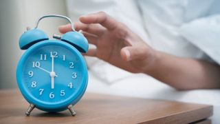 Woman hitting snooze on blue alarm clock