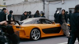 Han hangs out on his orange and black Mazda in The Fast and the Furious: Tokyo Drift