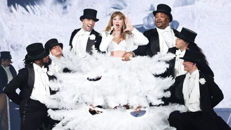 Taylor Swift performing with male dancers in suits as they cover her in large white feathered fans