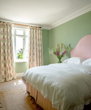 A green bedroom with floral curtains and a pink bed with white sheets