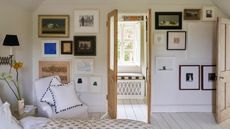 Bright bedroom with a gallery wall and bare wooden doors open to reveal a seated nook with window bench, cushion and white, crittal window