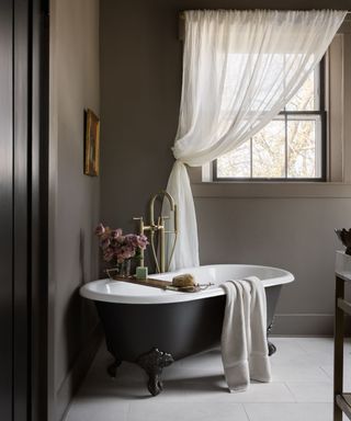 A brown bathroom with a claw foot bathtub in the corner and limestone tile floors