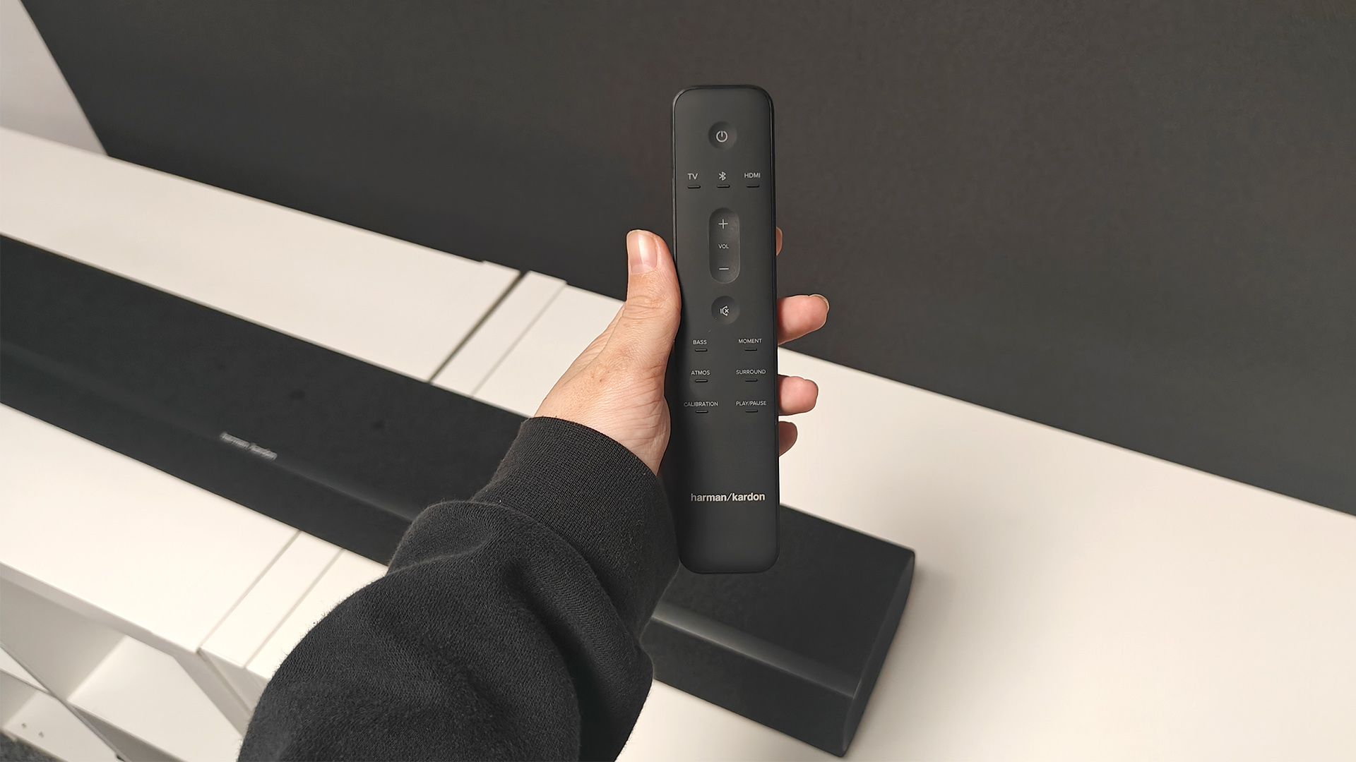 Harman Kardon Enchant 900 soundbar with remote held in hand above