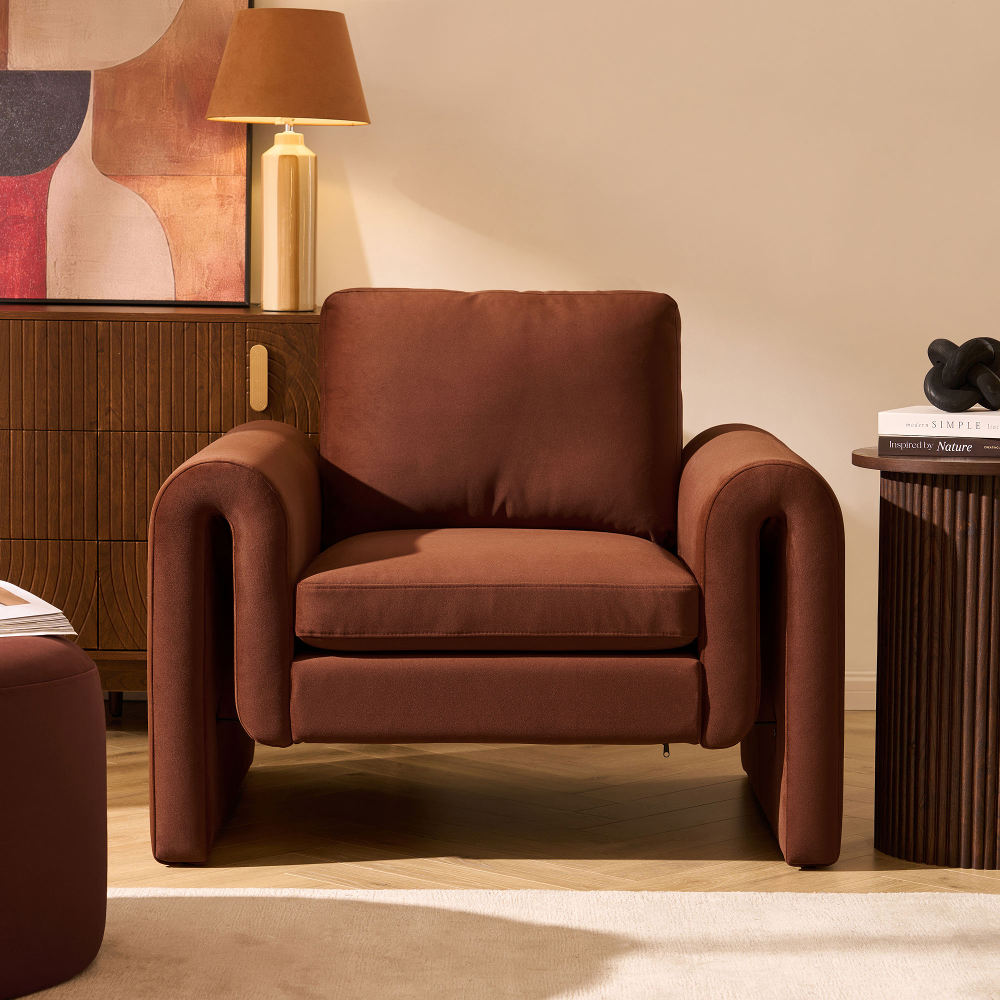 Terracotta armchair with curved arms, beige walls and wooden furniture around it