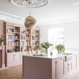 kitchen area with book shelves and white wall and pink counter with white countertop and ladder