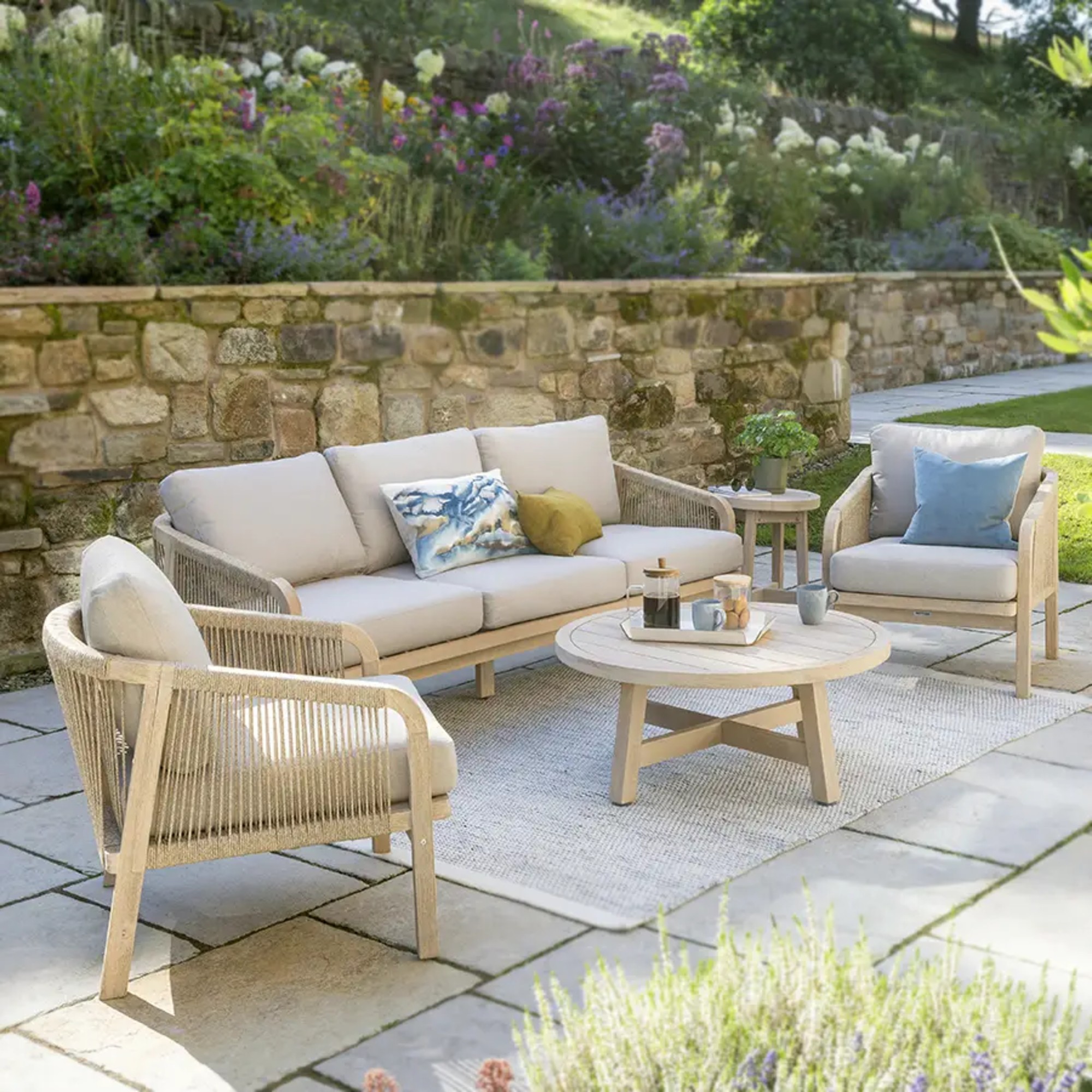 The Kettler Cora Rope 3-Seater Garden Sofa with two matching chairs and coffee table in a garden