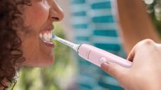 Philips Sonicare DiamondClean review: woman brushing teeth with pink electric toothbrush