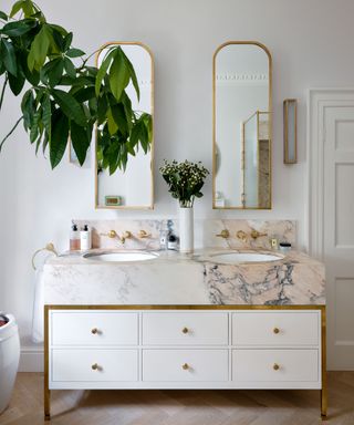 white bathroom with his and hers pink marble and white washstand and gold mirrors