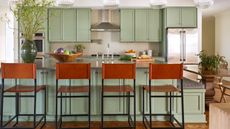 Green kitchen cabinet ideas exampled with sage base and wall green cabinets, tan and black bar stools, fluted glass pendant lights, vase with foliage, hardwood floor