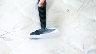 How to clean a mattress: a person uses a steam cleaning on a mattress