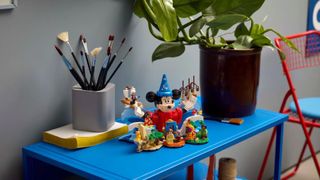 Lego Magic of Disney set on a blue table alongside a pot plant and paintbrushes