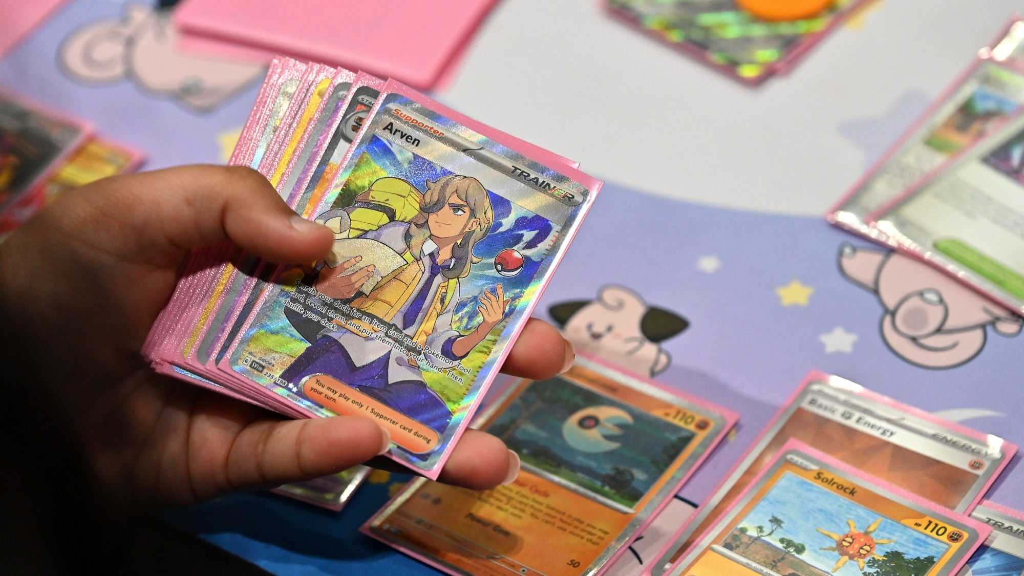 A competitor holds a deck showing an Arven card as they play the Pok&eacute;mon Trading Card Game 