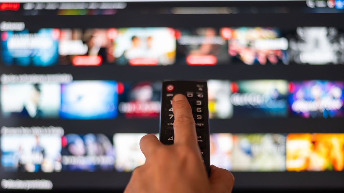 A person pointing a remote at a TV, blurred in the background is the Netflix interface