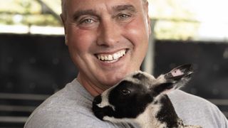 Dave Nicholson in a grey shirt holding a black and white lamb for Summer on the Farm